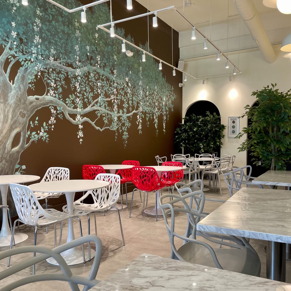 Cafe interior with a large tree mural, white and red chairs, and marble-top tables.