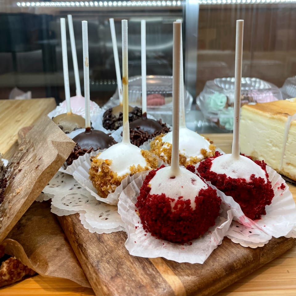 Assorted cake pops, including red velvet and chocolate, displayed on a wooden board at Kudo Society.