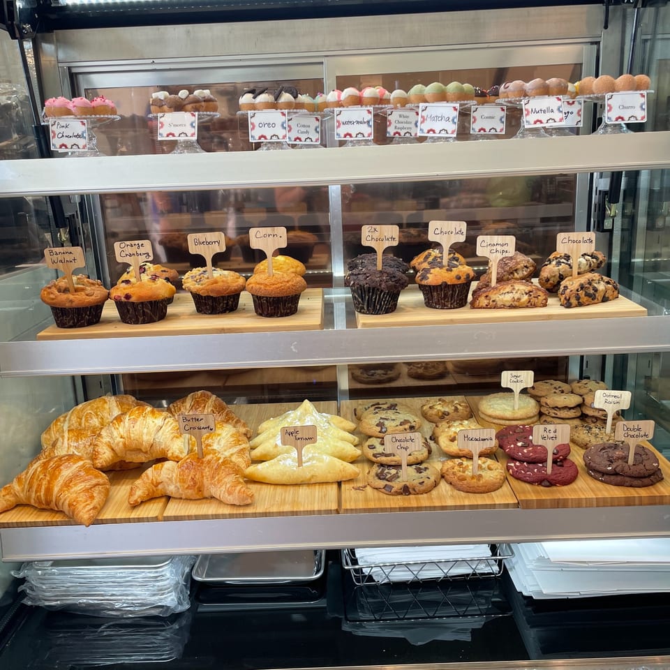 A display case at Kudo Society cafe filled with various muffins, cookies, croissants, and mini donuts.