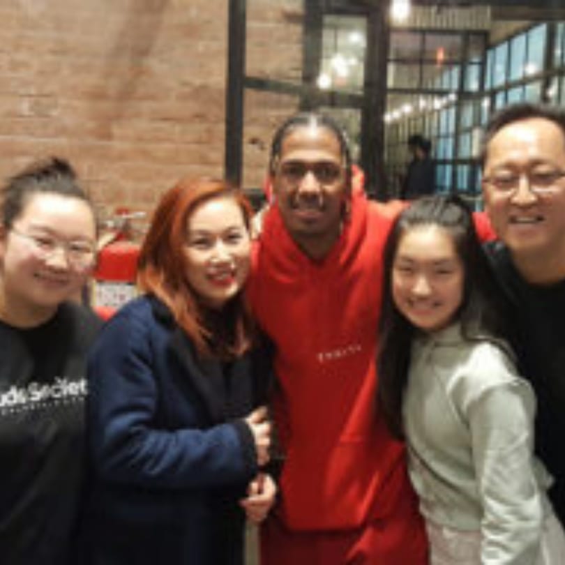 Five smiling people, including a man in a red hoodie, pose together inside Kudo Society cafe.