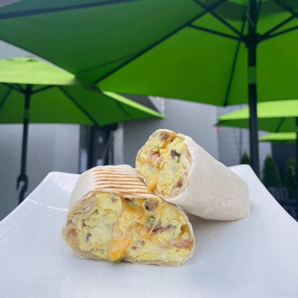 Kudo Society's breakfast burrito, cut in half, filled with scrambled eggs, cheese, and meat, on a white plate.