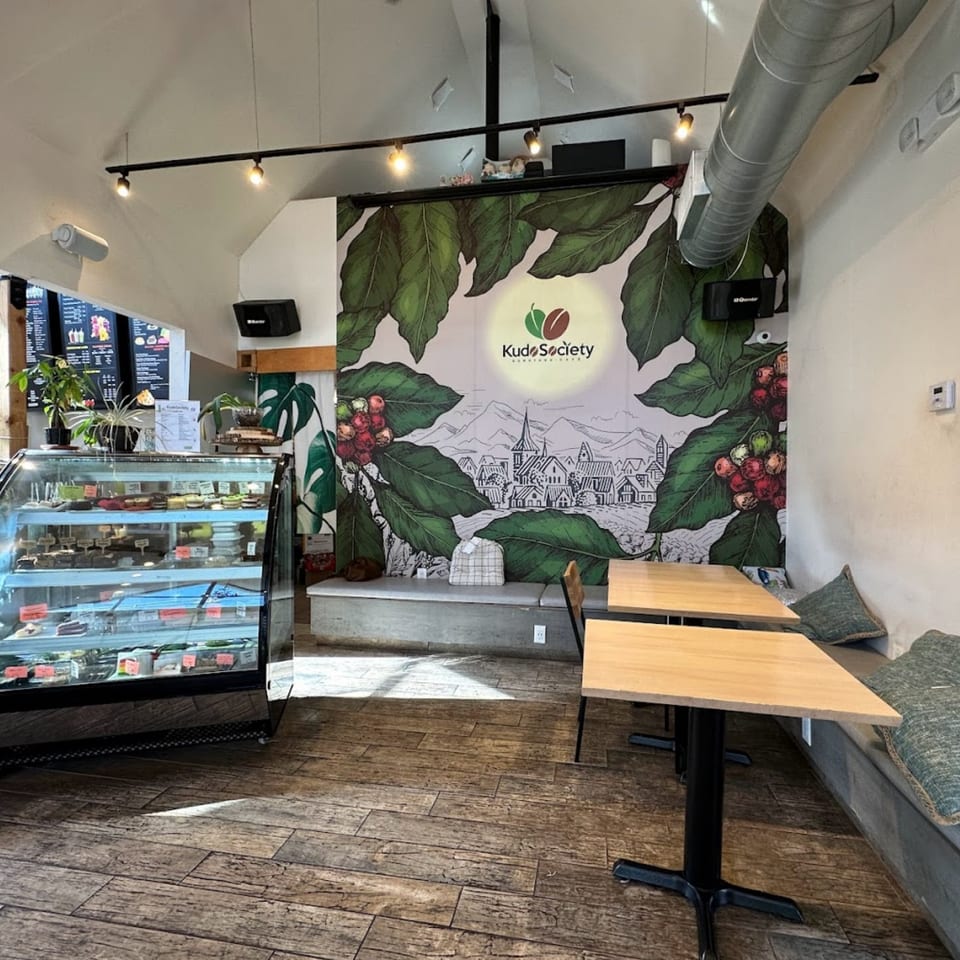 Interior of Kudo Society cafe with a dessert display case, tables, and a large coffee bean mural.