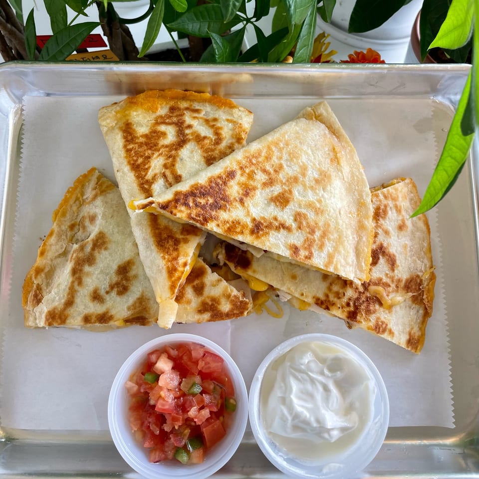 Golden-brown quesadilla triangles with melted cheese, served with salsa and sour cream on a metal tray.