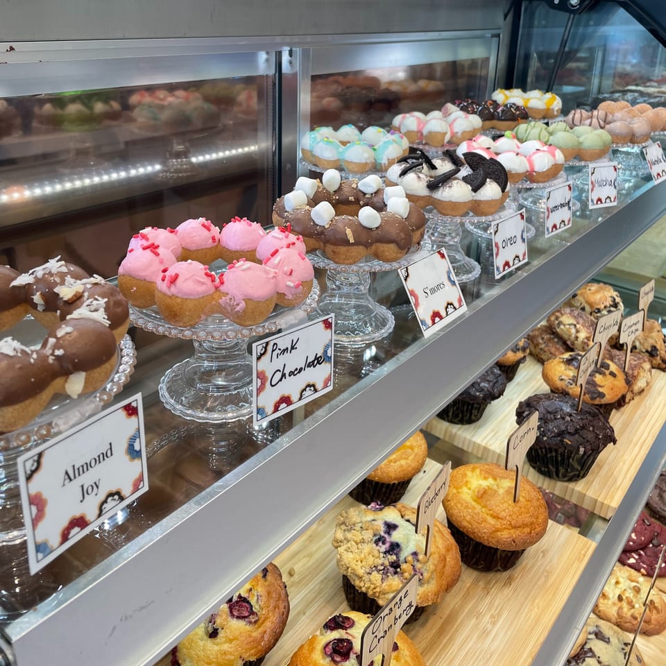 A display case at Kudo Society cafe filled with colorful mochi donuts and various muffins.
