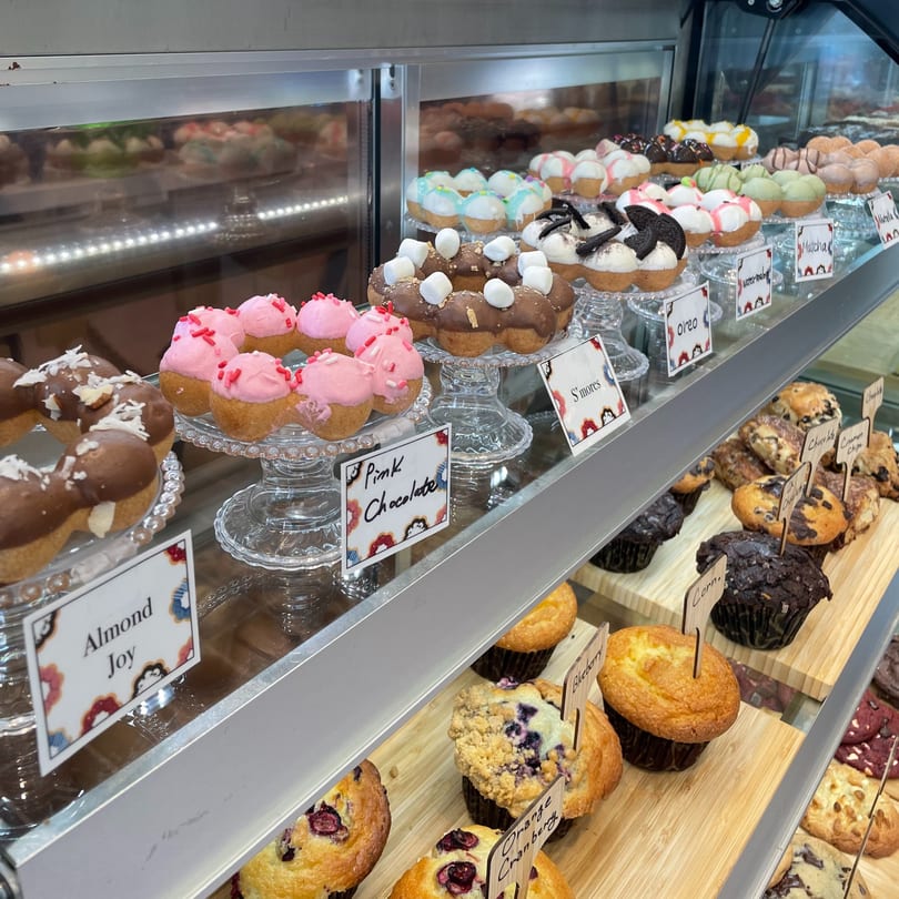 A display case at Kudo Society cafe filled with colorful mochi donuts and various muffins.