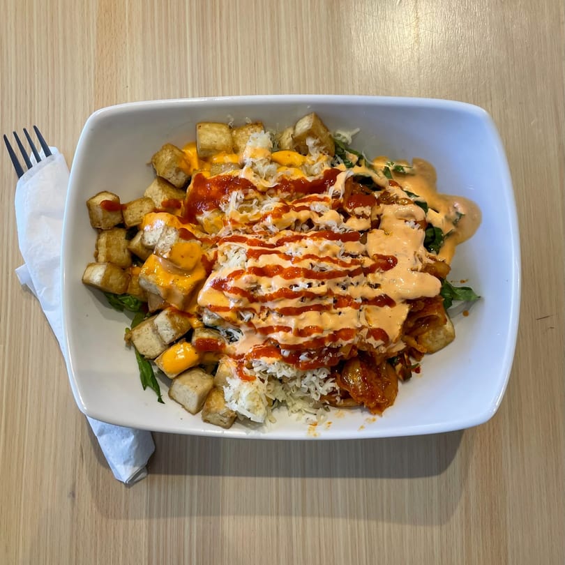 Kudo Society's colorful bowl with tofu, rice, kimchi, and various sauces on a wooden table.